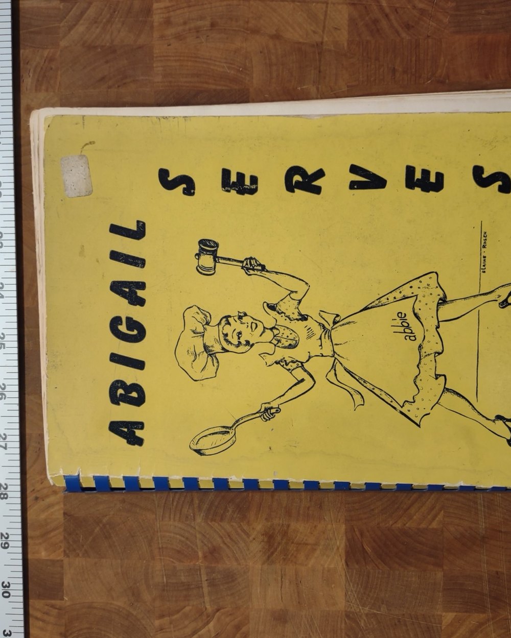 Yellow spiral-bound cover of Abigail Serves, with a line drawing of a cook in an apron