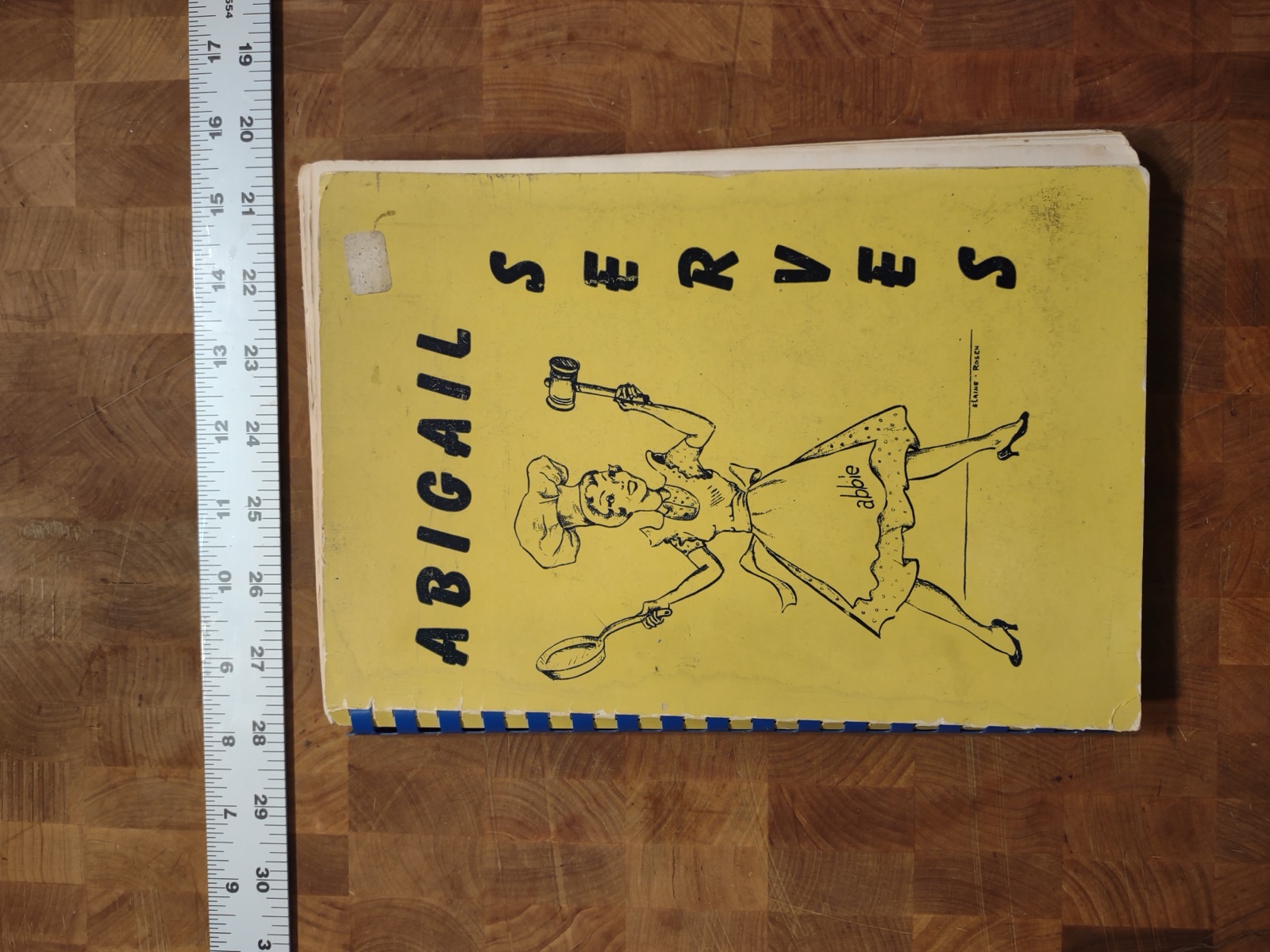 Yellow spiral-bound cover of Abigail Serves, with a line drawing of a cook in an apron