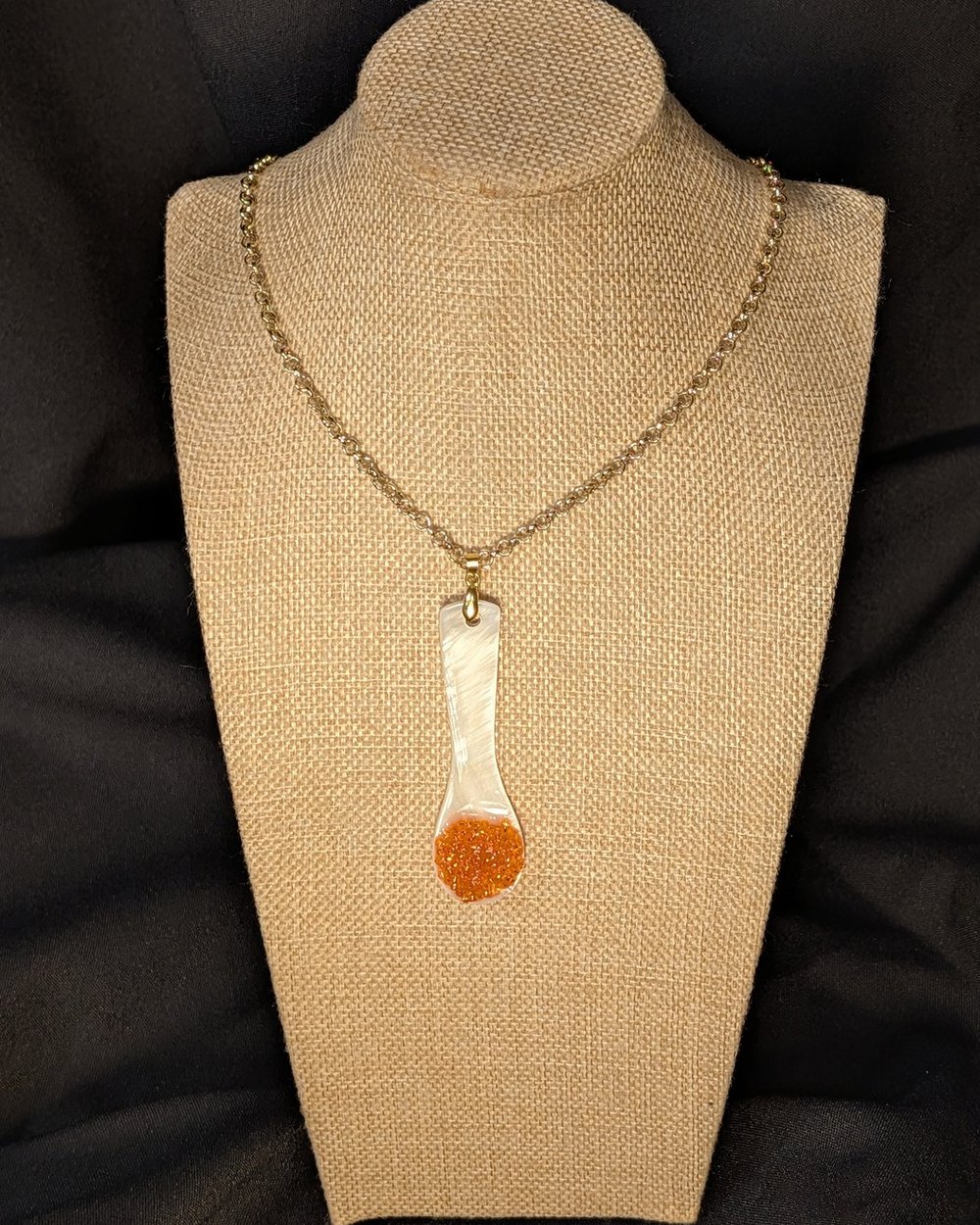 Caviar Spoon Necklace No. 3 — mother-of-pearl spoon with a salmon-orange bowl on a gold-tone chain, on a burlap display bust