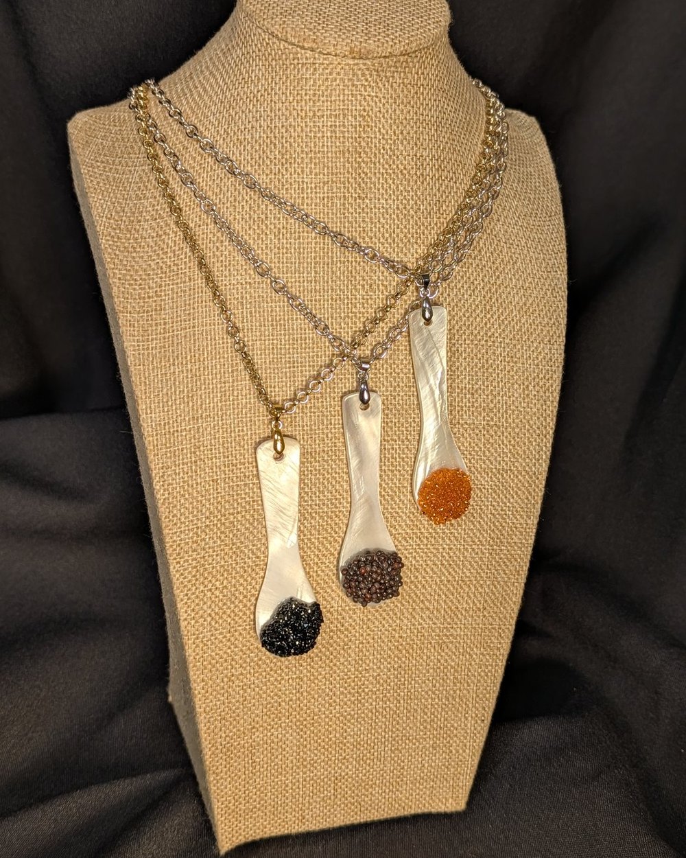Three caviar spoon necklaces layered at staggered lengths on a burlap bust