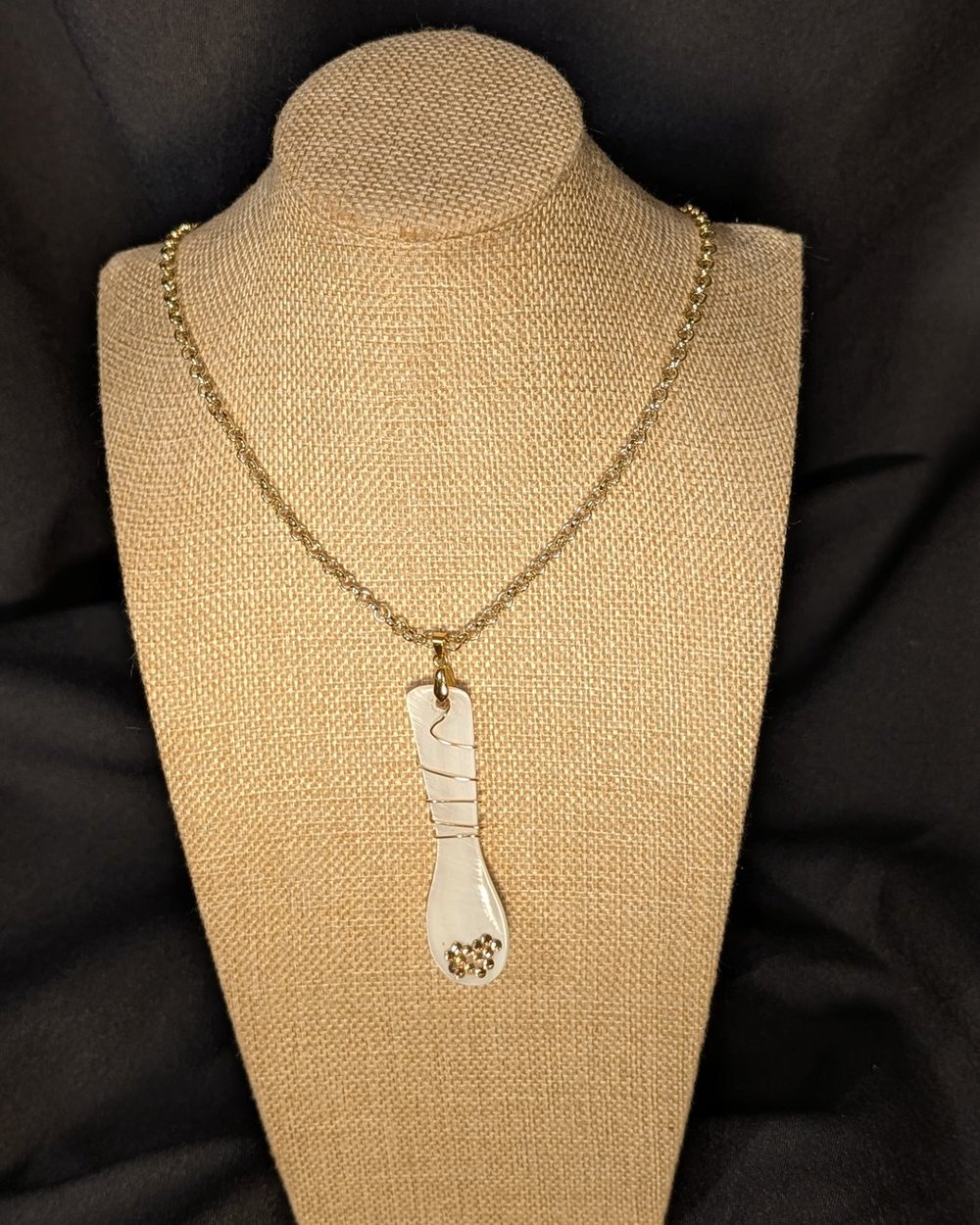 Caviar Spoon Necklace No. 8 — mother-of-pearl spoon with a pale pearl bowl and a wrapped handle on a gold-tone chain, on a burlap display bust